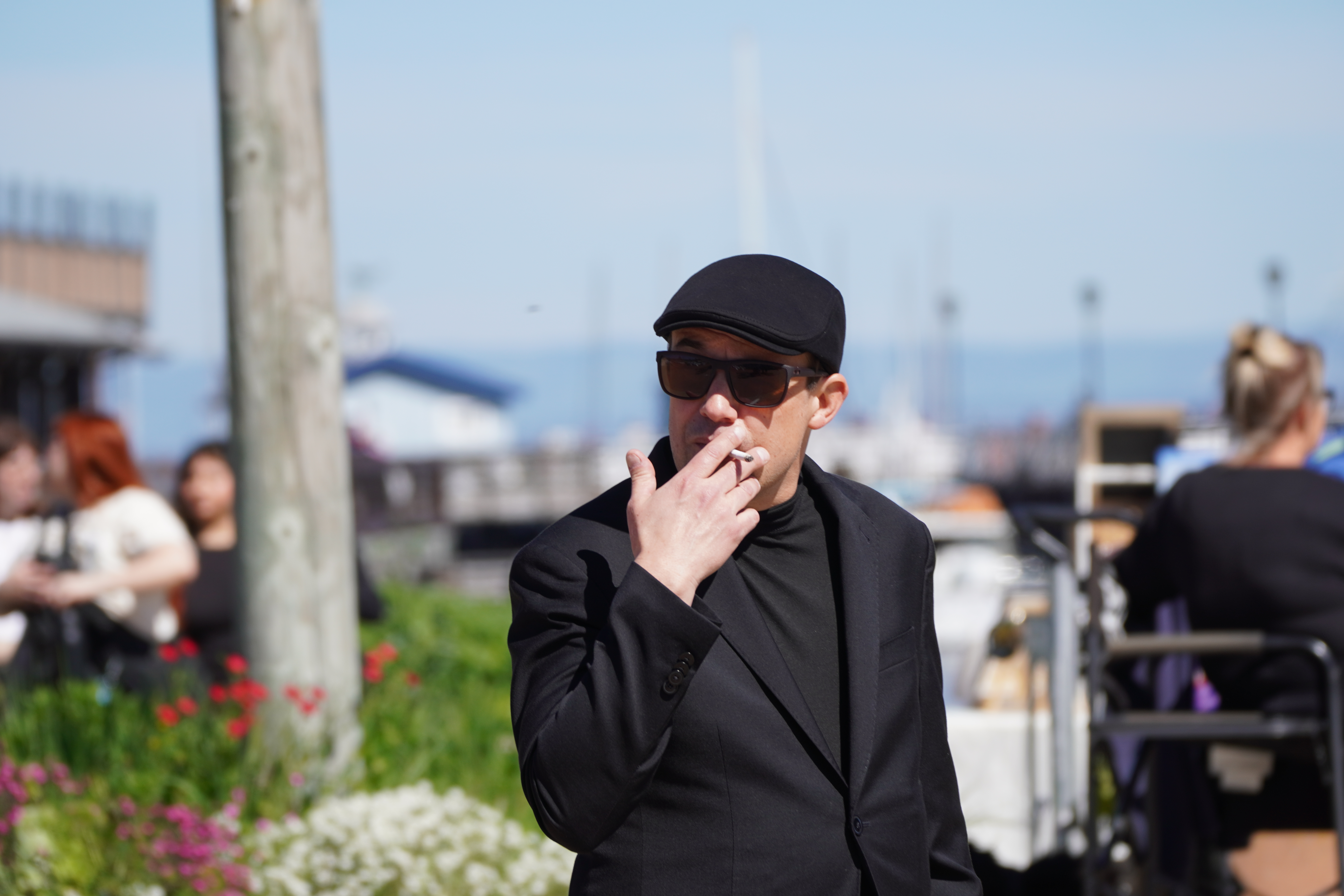 Street portrait of a man in dark clothing and sunglasses smoking outdoors
